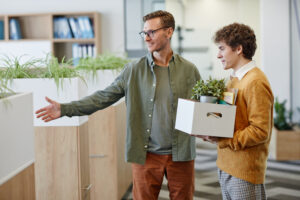 A smiling mentor facilitates employee onboarding by welcoming a young man to his new job.