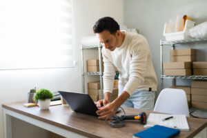A small business owner at a desk with a laptop, surrounded by office supplies and storage boxes, learning how to secure customer data.