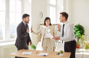 A tense office scene depicting business partner conflicts. A woman in a beige suit stands between two men, attempting to mediate their argument.