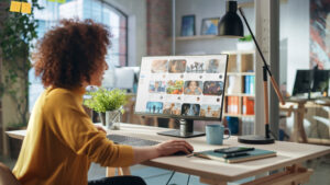 A small business owner in a modern office, wearing a yellow sweater, focused on a computer screen displaying digital content, researching copyright laws on social media.