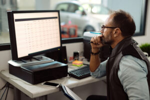 Focused middle-aged man in glasses and a vest reviews financial data on a computer screen at a well-organized desk, symbolizing the importance of avoiding retirement planning mistakes for small business owners.