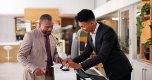 A hotel concierge welcomes a guest at a reception desk, representing the importance of comparing the top hotel loyalty programs for small businesses.