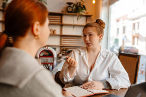 A cafe owner takes notes as she conducts job interviews in a cozy cafe setting.