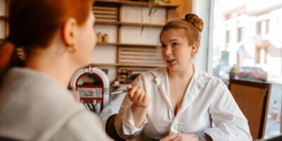 A cafe owner takes notes as she conducts job interviews in a cozy cafe setting.