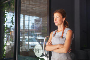 A small business owner stands confidently by the entrance to her cafe, ready to recession-proof her business finances.