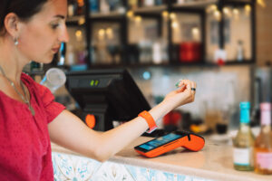 A woman at a bar counter demonstrates the value of small business tech by holding her smartwatch over a card reader to quickly and efficiently pay her bill.