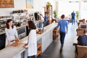 A modern café scene illustrating the 80/20 rule, where a small group of loyal customers drives the majority of revenue. The image shows a bustling environment with a customer interacting with staff at the counter, emphasizing the importance of focusing on high-value customers to optimize revenue from top customers.