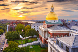 Sunset view of the Massachusetts State House with its iconic golden dome, surrounded by lush greenery and urban architecture, symbolizing the complexity of state labor laws in the region.