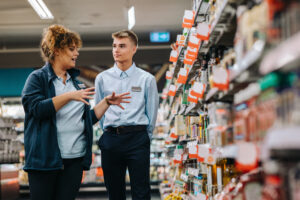 Two retail employees, a woman and a young man, engaged in a discussion in a store aisle, illustrating effective communication and training practices for hiring and managing underage employees.