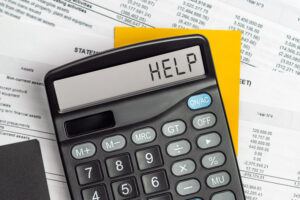 A black calculator displaying the word "HELP" sits on top of financial documents and a yellow notepad, symbolizing the challenges of small business tax preparation.