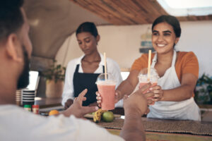 A smoothie shop employee hands two drinks to a customer at a busy counter, illustrating summer pricing strategies for small businesses during the seasonal rush.