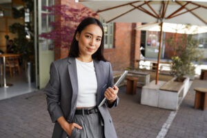 Female small business owner holding a laptop outside a café, representing women-owned entrepreneurship and the Hey Helen Grant for small business funding.
